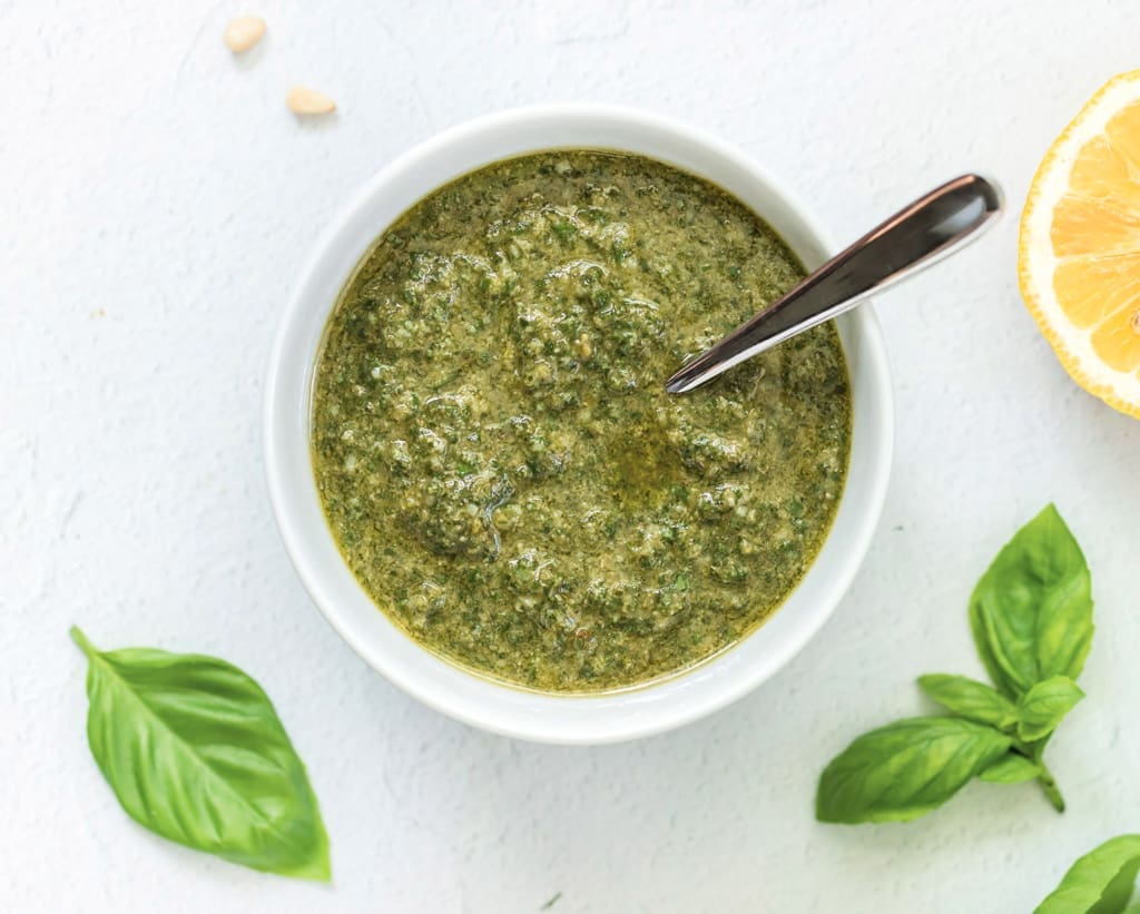 Basil pesto in a white bowl with a silver spoon.