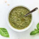 Basil pesto in a white bowl with a silver spoon.