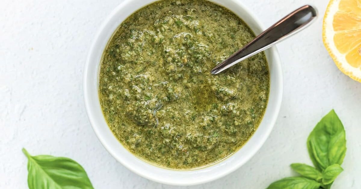 Basil pesto in a white bowl with a silver spoon.