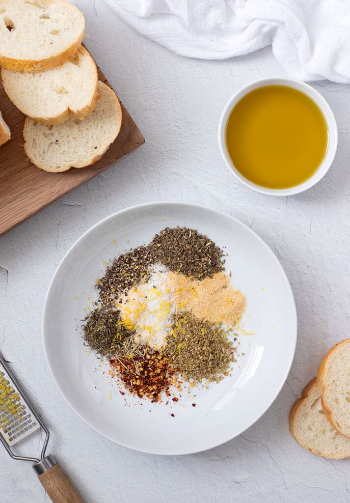 Seasonings in a white bowl next to bread and a dish of oil.