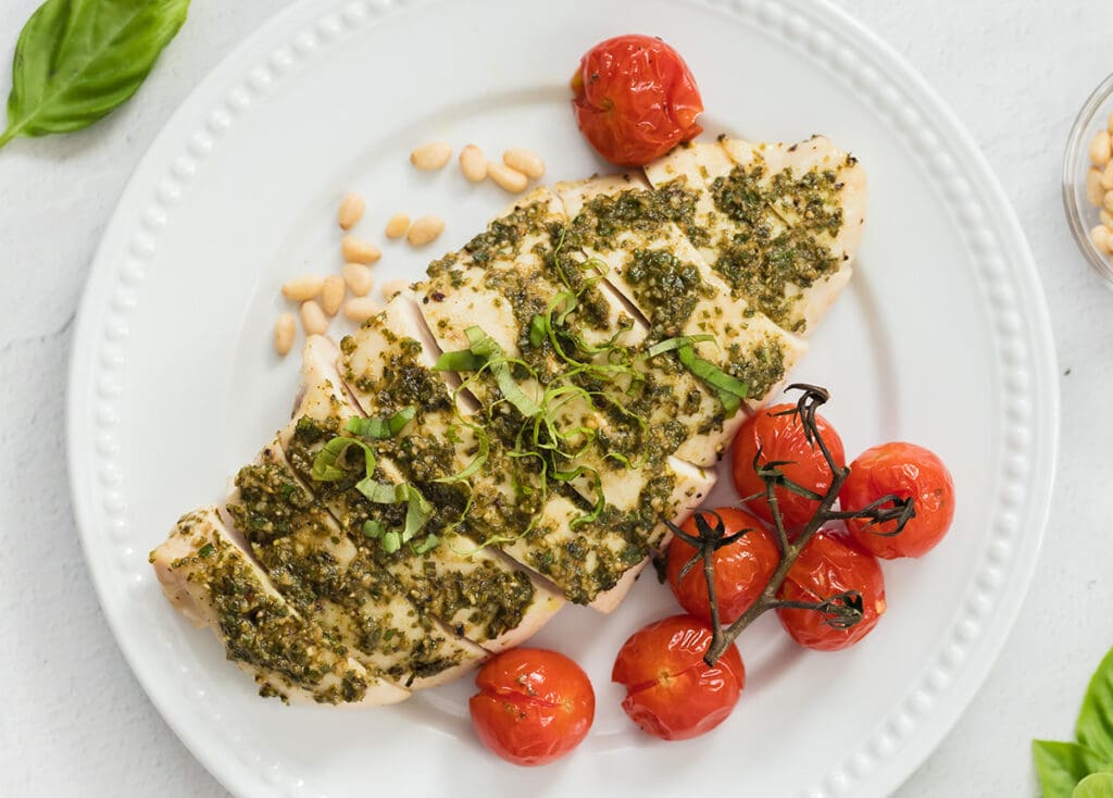 Pesto Chicken on a white plate with tomatoes.