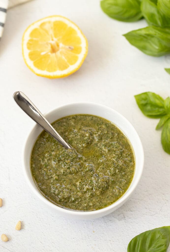 Small bowl of pesto sauce and slice of lemon.