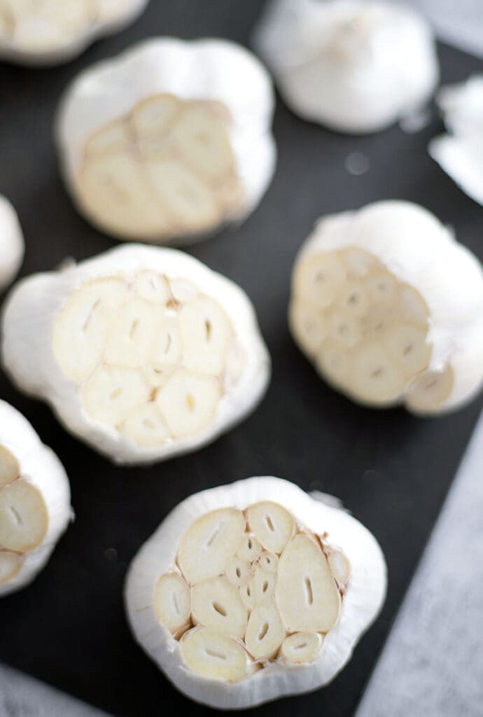 Cut garlic bulbs on a black cutting board.