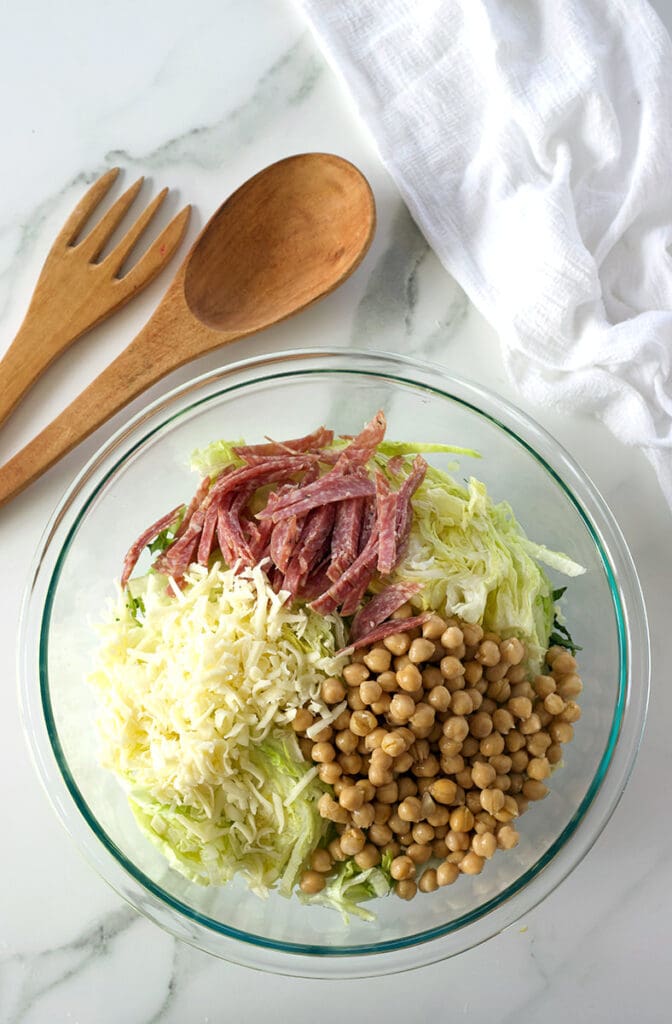 Variety of ingredients in a clear bowl next to wooden utensils.