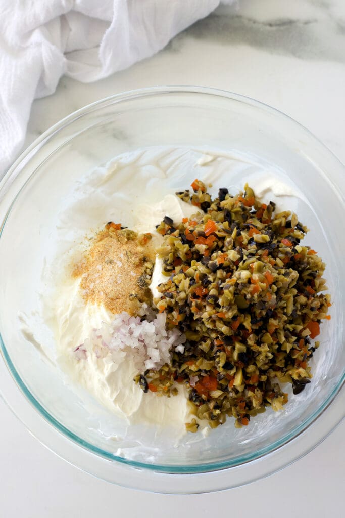 green and black olives on top of cream cheese in a glass bowl.