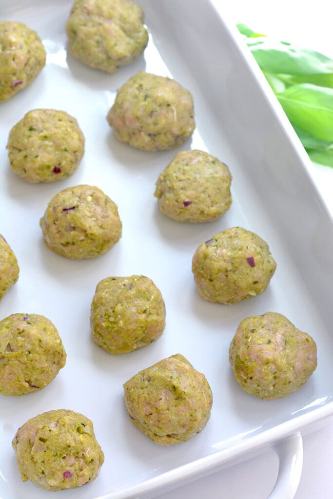 Baking sheet with rows of uncooked meatballs.