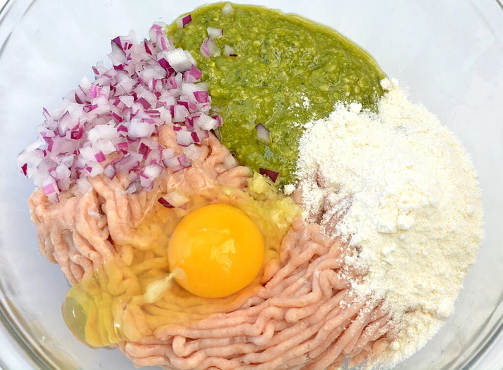 Clear bowl with ground chicken, eggs and pesto sauce.