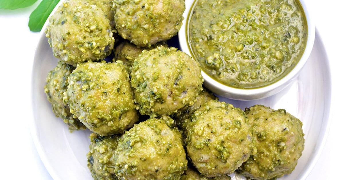 White plate full of pesto meatballs with a side of pesto.
