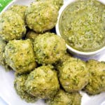 White plate full of pesto meatballs with a side of pesto.