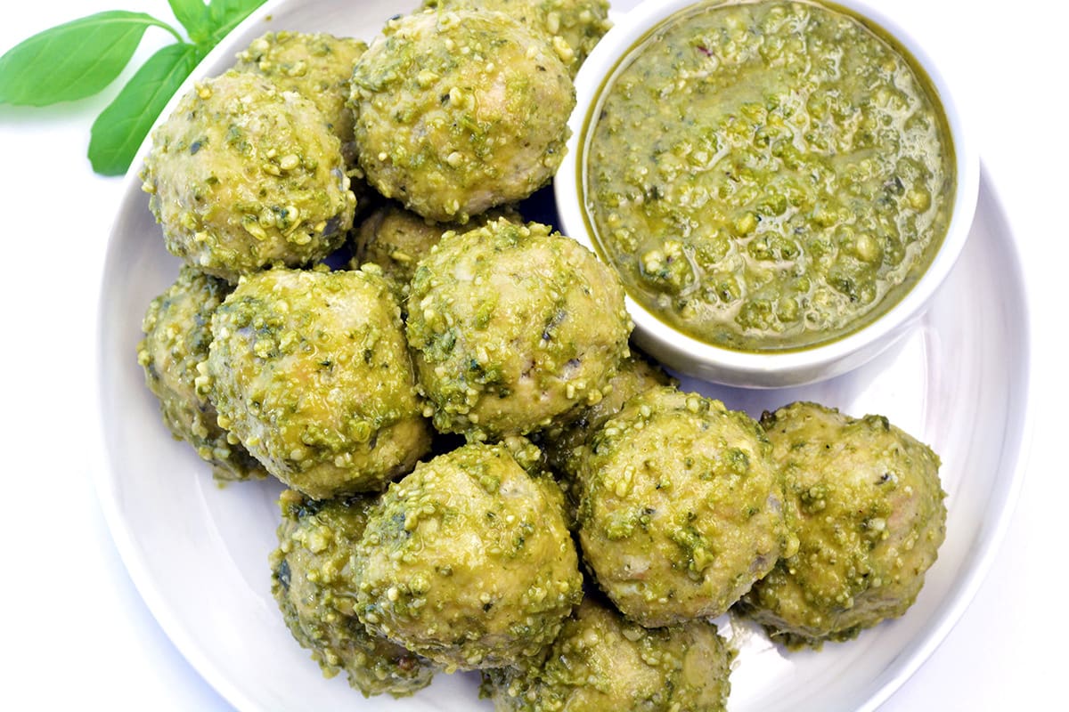 White plate full of pesto meatballs with a side of pesto.