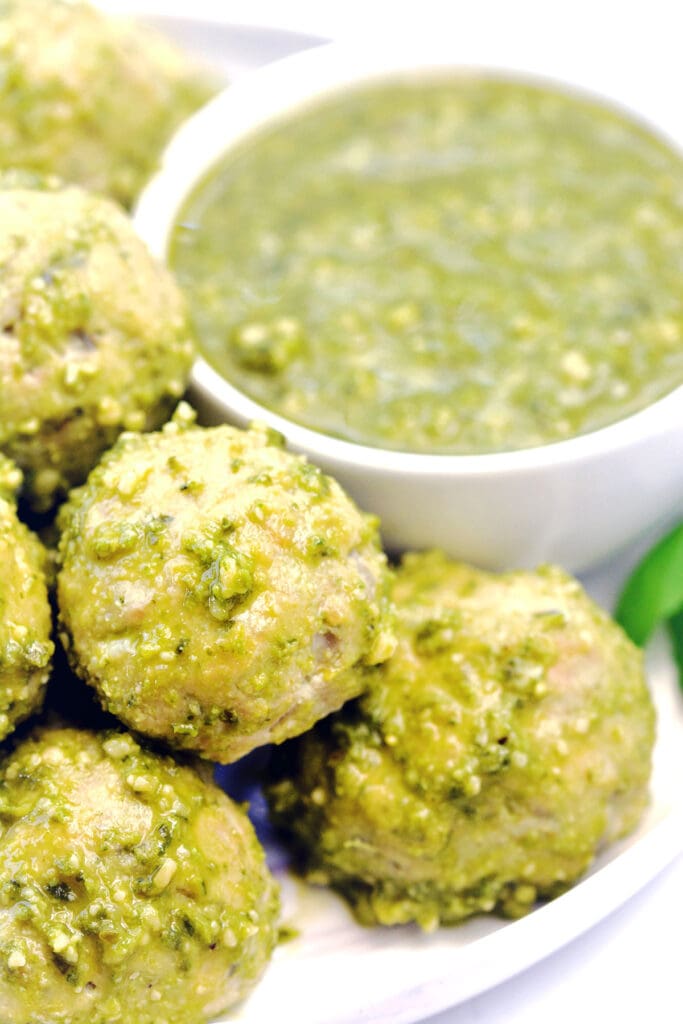 White plate full of pesto meatballs with a side of pesto.