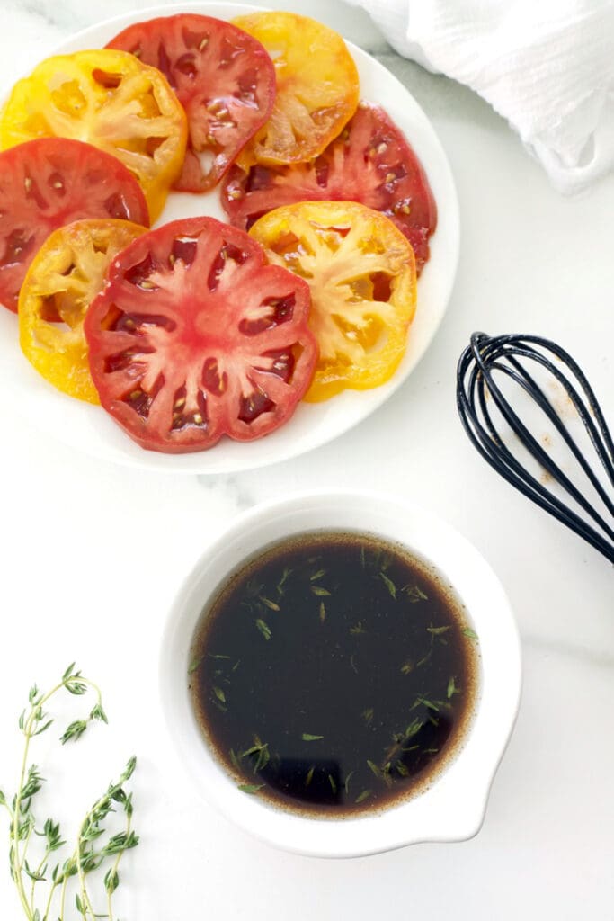 Container of balsamic marinade next to a plate of sliced produce.